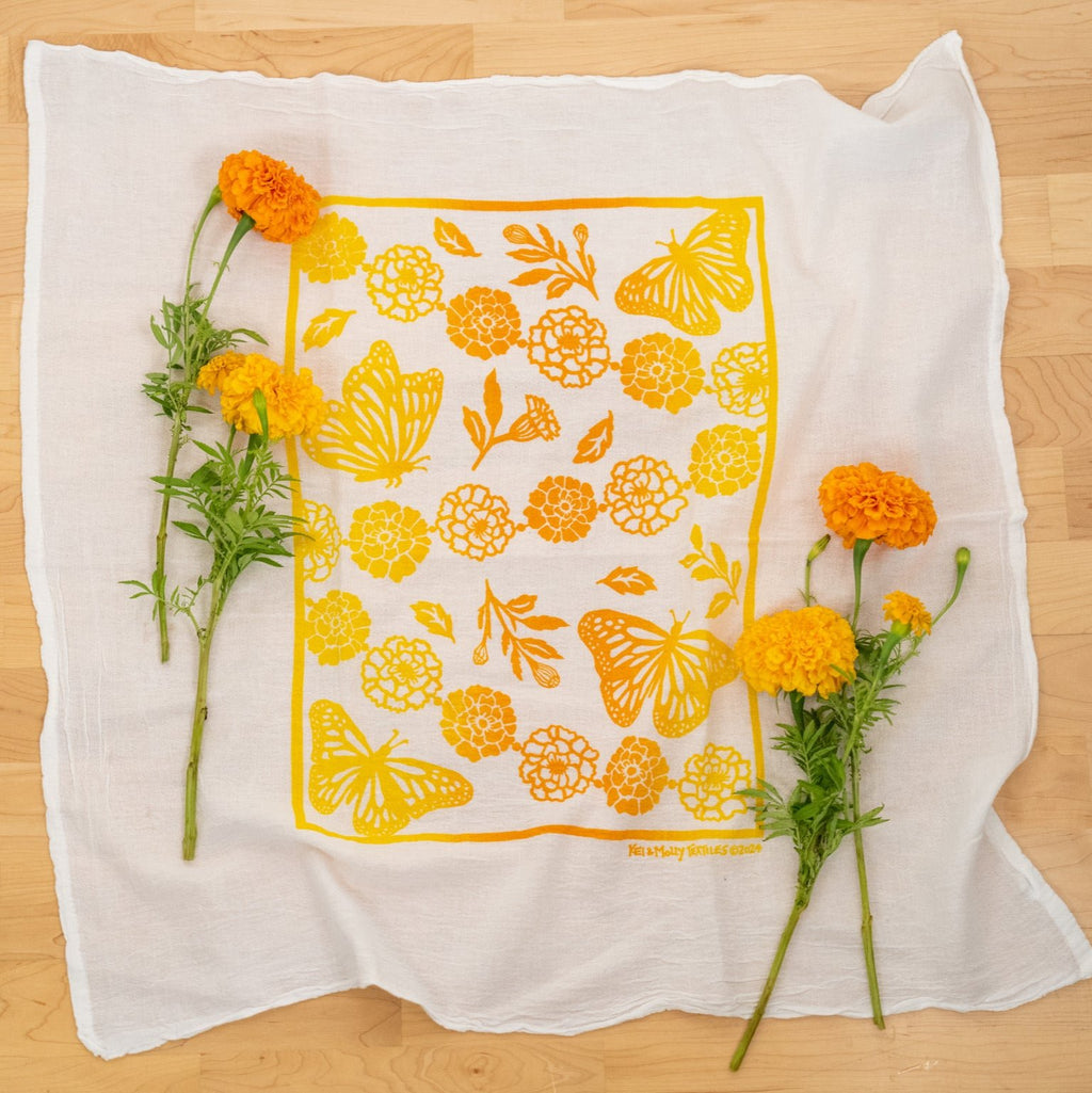 Kei & Molly Flour Sack Dish Towel full view, Monarchs & Marigolds design in two-tone yellow and squash with marigold props