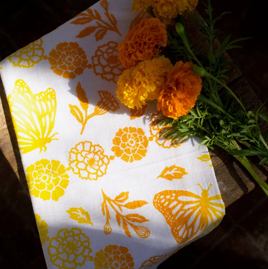 Kei & Molly Flour Sack Dish Towel full view, Monarchs & Marigolds design in two-tone yellow and squash with marigold props