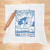 Kei & Molly's Slow Down Flour Sack Dish Towel in Steel Blue, front view with rolling pin prop.